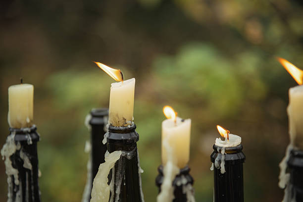 Soft flames dance atop soaked candles placed on dark bottles. The background is blurred, creating a mysterious and peaceful atmosphere as twilight descends.
