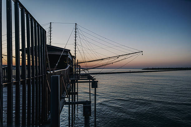 Trabocco, a traditional fishing structure, extending into the calm Adriatic Sea at sunset, featuring intricate wooden platforms and nets against a gradient sky as dusk settles over the water.