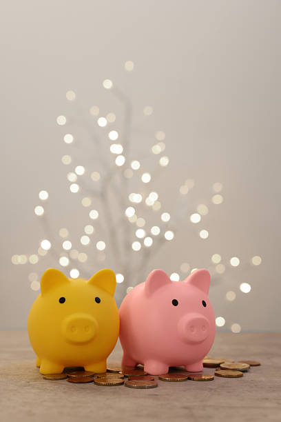 istock Piggy banks and coins on grey table against blurred lights 2246053151