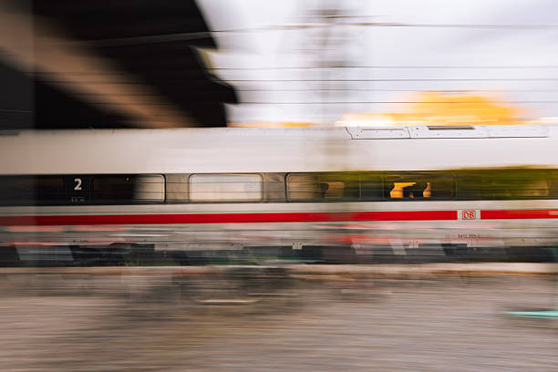 Berlin, Germany – October 29, 2025: Deutsche Bahn ICE high-speed train captured in motion at Berlin Ostkreuz. The image shows the side view of the train moving through the platform area with visible motion blur and reflection of city lights.