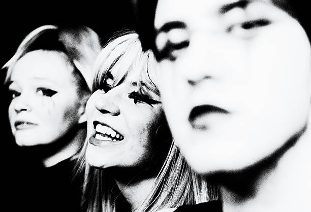 Expressive black-and-white portrait of three young musicians inspired by the Post-Punk and New Wave era. Strong contrasts, smudged eyeliner, and a spontaneous smile capture the raw energy of an underground performance — balancing melancholy, rebellion, and joy.