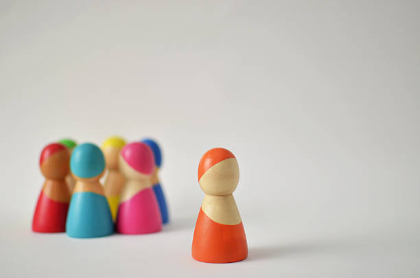 istock Orange wooden figure standing apart from colorful group 2246055971