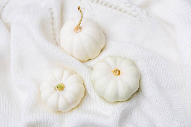 Three small white pumpkins rest on a soft white textured fabric.