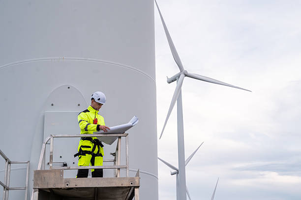 istock A man is standing on a platform next to a wind turbine. He is wearing a yellow jacket and a hard hat. Professional engineer in safety harness conducting inspection at a wind turbine farm. 2246060090