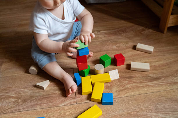 istock A young child is focused on stacking vibrant wooden blocks on a wooden floor, using hand-eye coordination and concentration. The scene illustrates early learning and playtime activities. 2246060664