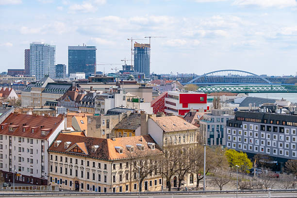 Bratislava cityscape featuring traditional and modern architecture. The image captures a mix of historical rooftops and contemporary skyscrapers, showcasing the iconic bridge and urban development