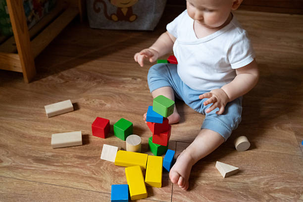 istock A young child is focused on stacking vibrant wooden blocks on a wooden floor, using hand-eye coordination and concentration. The scene illustrates early learning and playtime activities. 2246060761