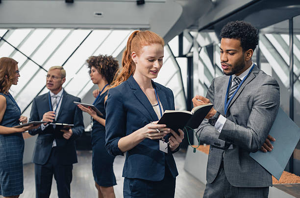 Business professionals exchanging notes and ideas in a modern office corridor, fostering a collaborative and energetic atmosphere. Colleagues are seen in conversation, highlighting teamwork and professional engagement.