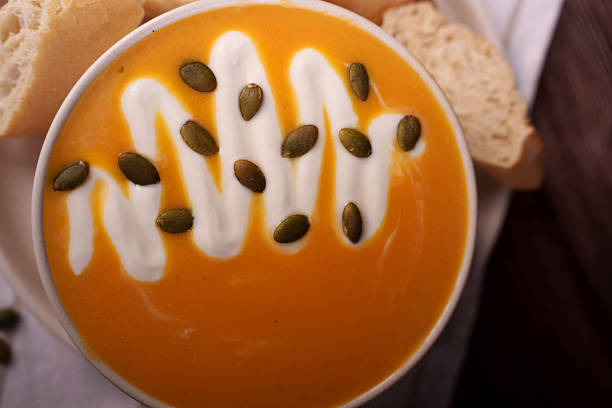 creamy pumpkin soup with drizzled cream and pumpkin seeds accompanied by rustic bread slices, captured in a warm and inviting culinary setting, brown, flavorful, nourishing, aesthetic, delightful