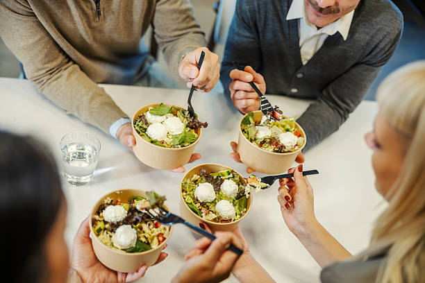 Group of business people eating fresh salads from eco-friendly containers during their lunch break at the office