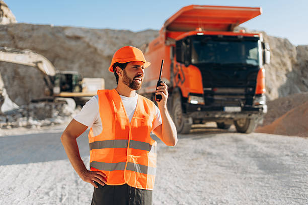 istock Confident Latin male construction supervisor wearing orange hard hat communicating via walkie talkie 2246066181