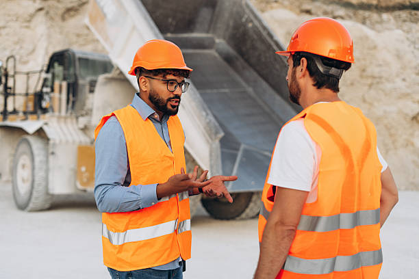 istock Two construction workers wearing orange safety vests and helmets at a quarry site near dump truck 2246066282