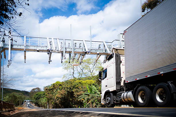 Freight trucks driving on a road equipped with multiple security and speed cameras for monitoring.