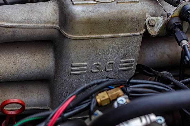 A detailed close-up view of a car engine compartment with the hood open, captured during a roadside breakdown on a sunny day. The image shows various automotive components including the car battery, radiator, hoses, and engine parts, emphasizing real-life vehicle maintenance, mechanical issues, and car troubleshooting scenarios. Ideal for illustrating concepts such as car repair, emergency assistance, travel problems, and automotive safety