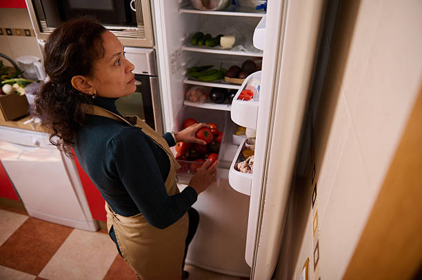 istock Woman in Apron Picks Fresh Tomatoes From Open Fridge in Bright Kitchen 2246072010