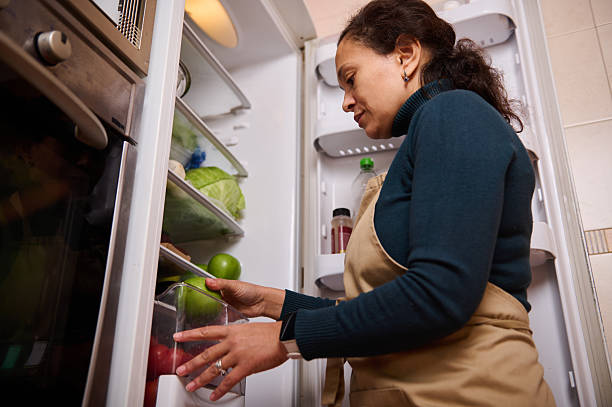 istock Woman in Apron Picks Fresh Produce From Open Refrigerator in Home Kitchen 2246072041