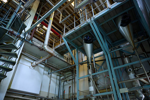 The equipment appears to be part of a processing or manufacturing facility, with visible stainless-steel piping systems, pumps, and vertical vessels. The walls and floor show signs of rust, wear, and discoloration, indicating age or heavy use.