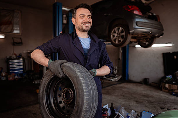 istock Mechanic smiles while holding a tire in a busy garage 2246078940