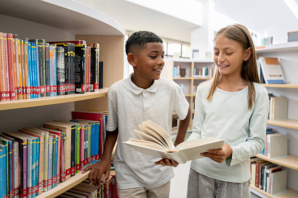 Happy Latin American students reading a book at the school library - education concepts