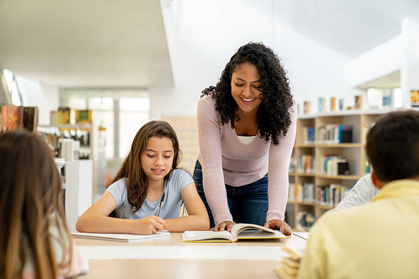 istock Happy teacher helping a young student while reading a book at the library 2246082315