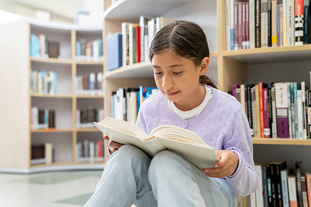 istock Happy schoolgirl reading a book at the library 2246082323