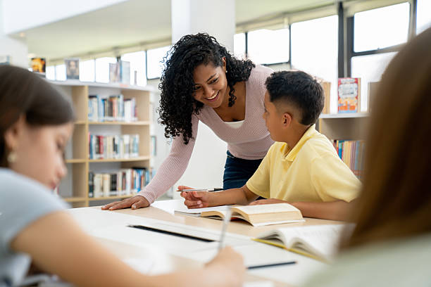 istock Happy teacher helping a schoolboy while studying at the library 2246082332