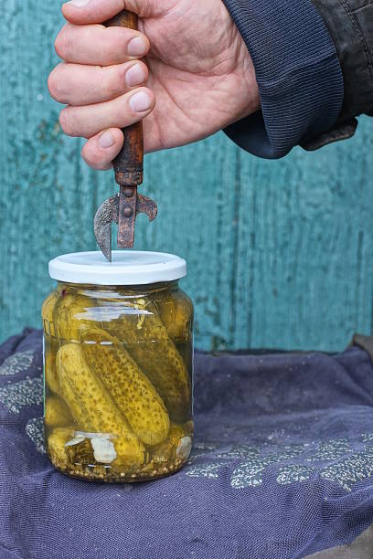 istock A hand with an old rusty can opener opens a white metal lid on a glass jar 2246082599