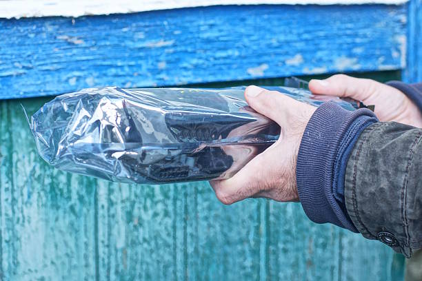 A man's hands hold one transparent plastic bag with a black package against the background of a wall on an autumn street