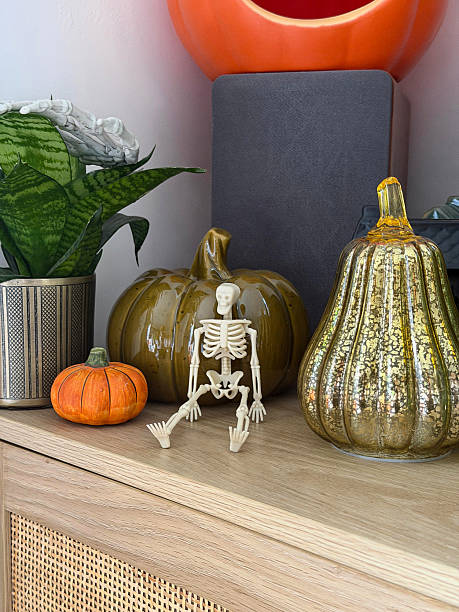 istock Close-up image Halloween decoration display arranged on wooden sideboard, stack of orange Jack O'lanterns on speaker, glazed china gourds and pumpkin, plastic skeleton, black model house, potted plants, focus on foreground 2246085792