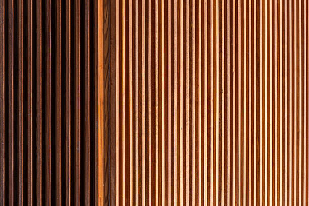 Luxury interior wall featuring vertical wood slats in a light natural finish.  Japandi style. The slats are evenly spaced with dark gaps between them, creating a clean, rhythmic pattern often used for acoustic and decorative purposes. A section of grey textured material on the right adds contrast and depth, enhancing the refined, contemporary design.