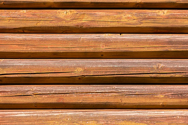 Horizontally stacked wooden logs with rich brown coloration, visible grain, and natural knots create a warm, rustic texture ideal for log cabin walls and traditional architecture. The cylindrical shape and parallel alignment emphasize handcrafted construction and organic charm. Perfect for use in interior design, building materials catalogs, or nature-themed visual projects.