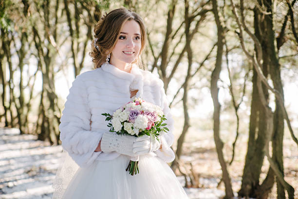The bride with a wedding bouquet is smiling in the winter forest