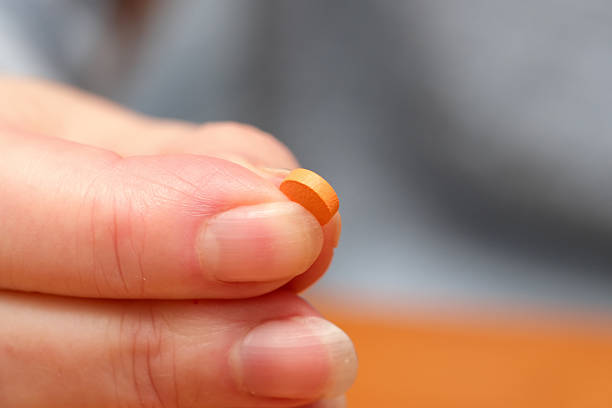 A hand gently holds a tiny orange tablet in clear focus, showcasing its detail.