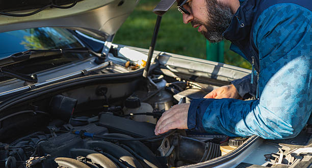 istock Man inspecting car engine under the hood in sunny outdoor setting 2246117260