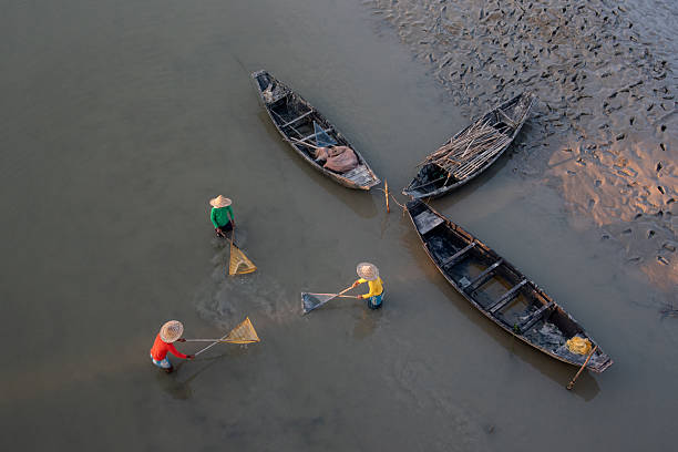 Top view of three unidentified men using fishing nets in shallow water