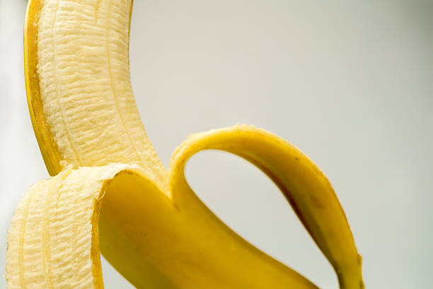 Peeled banana half revealing vibrant yellow pulp on white background ,fresh, ripe, natural snack perfect for healthy eating and desserts