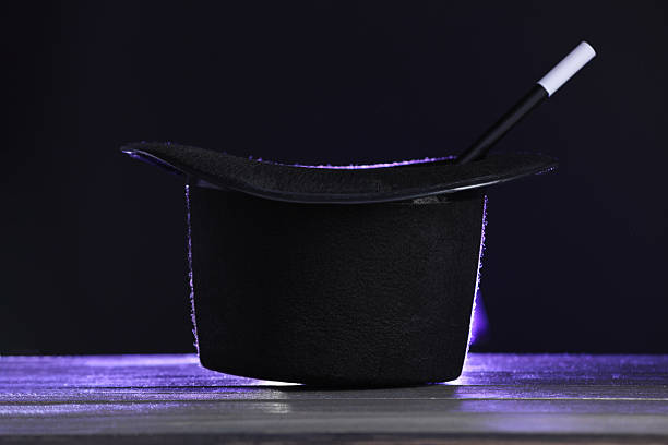 istock Magician's hat and wand on wooden table against black background 2246120486