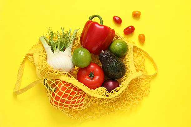 String bag with fresh vegetables and fruits on yellow background, flat lay