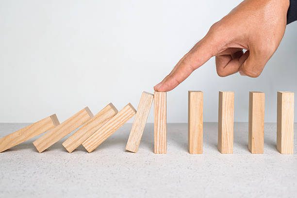 istock male hand stop falling wooden blocks. domino effect or risk protection strategy concept 2246122218