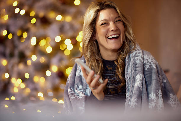 Cheerful woman having fun while using cell phone during New Year's at home.