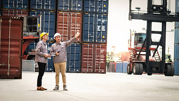 istock Two men standing in front of a large container ship. One of them is pointing at something. Scene is serious and focused 2246125217