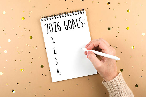 istock Hand holding a white pen, writing on a blank notepad titled 2026 Goals, surrounded by golden confetti, symbolizing planning 2246125462