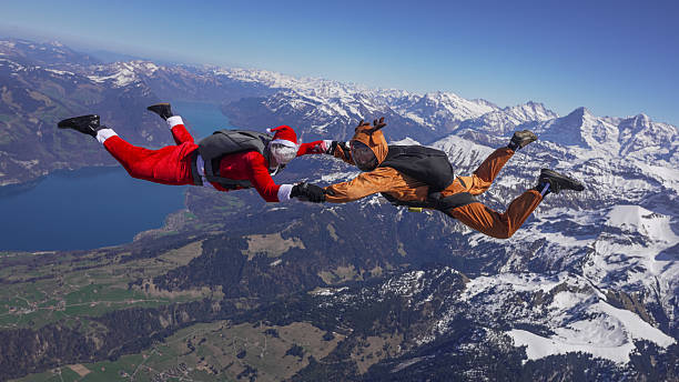 Skydivers/Free fall fliers, dressed as Santa Claus and Reindeer, hold hands mid-air above snowcapped mountains, Bern Canton