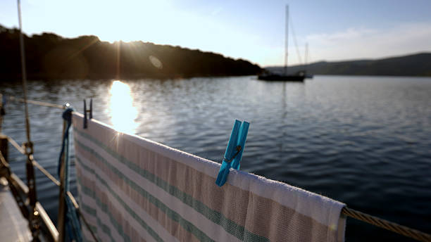 Laundry dries on sun on sailboat, harbour and sailboat in distance, morning light