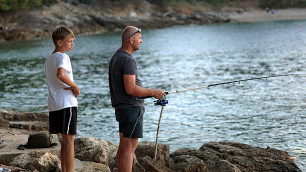 istock Father and son fish from rocky coastline 2246130041