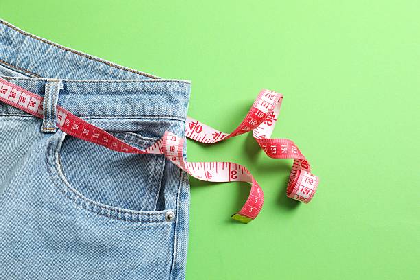 istock Blue jeans with a measuring tape instead of a belt on a colored background 2246134580