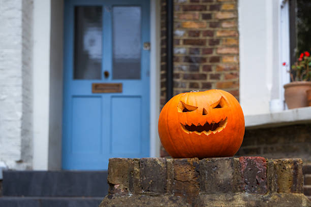 A carved pumpkin perched on a wall outside a residential house in the city. The pumpkin signals that the house is willing to receive trick-or-treaters.
