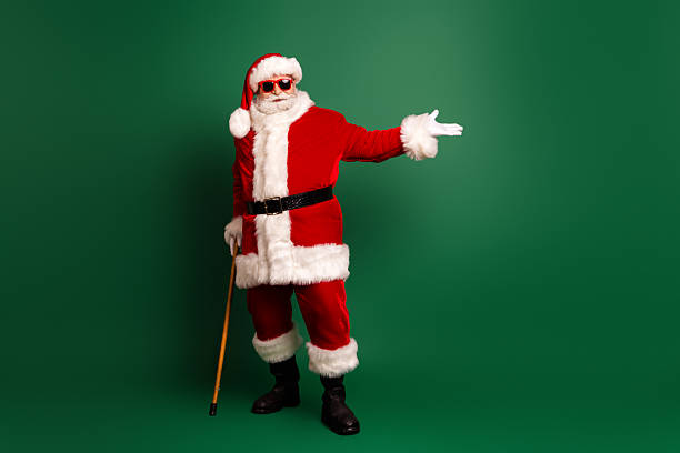 istock Santa in red costume with white fur belt and cane poses on green studio backdrop inviting festive cheer and holiday magic 2246137538