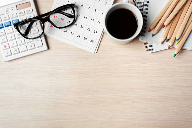 A workspace arranged with a calendar, coffee, glasses, and colored pencils on a wooden table