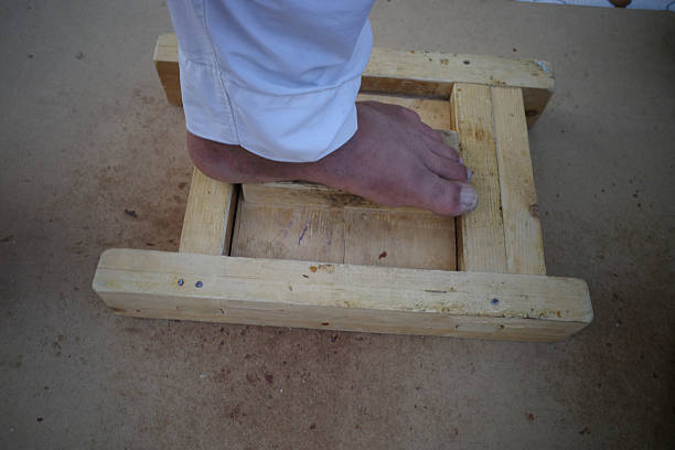 A foot placed on a wooden device, possibly for exercise or therapy, with a simple wooden frame